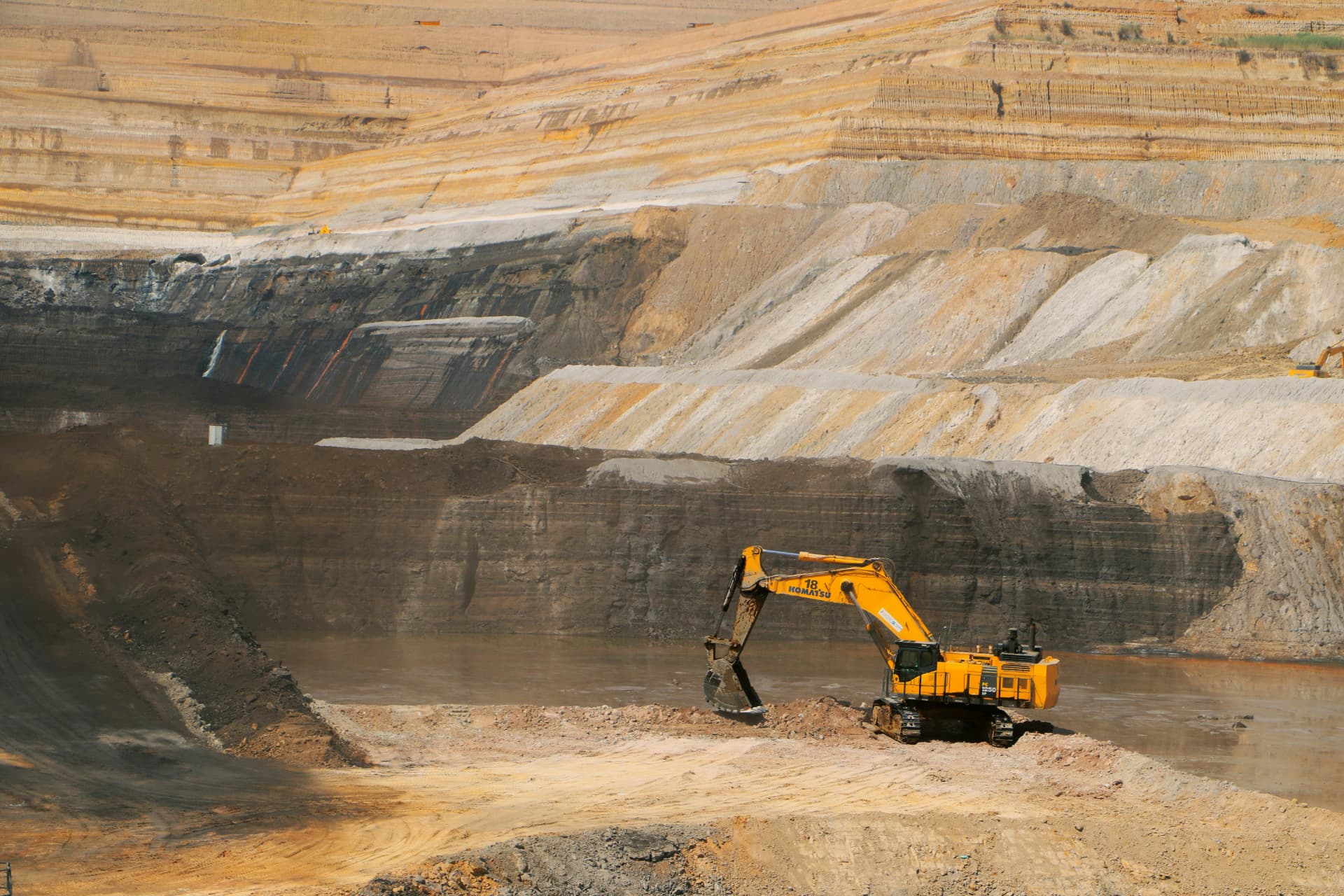Yellow hydraulic excavator working on a bench in a terraced open-pit mine